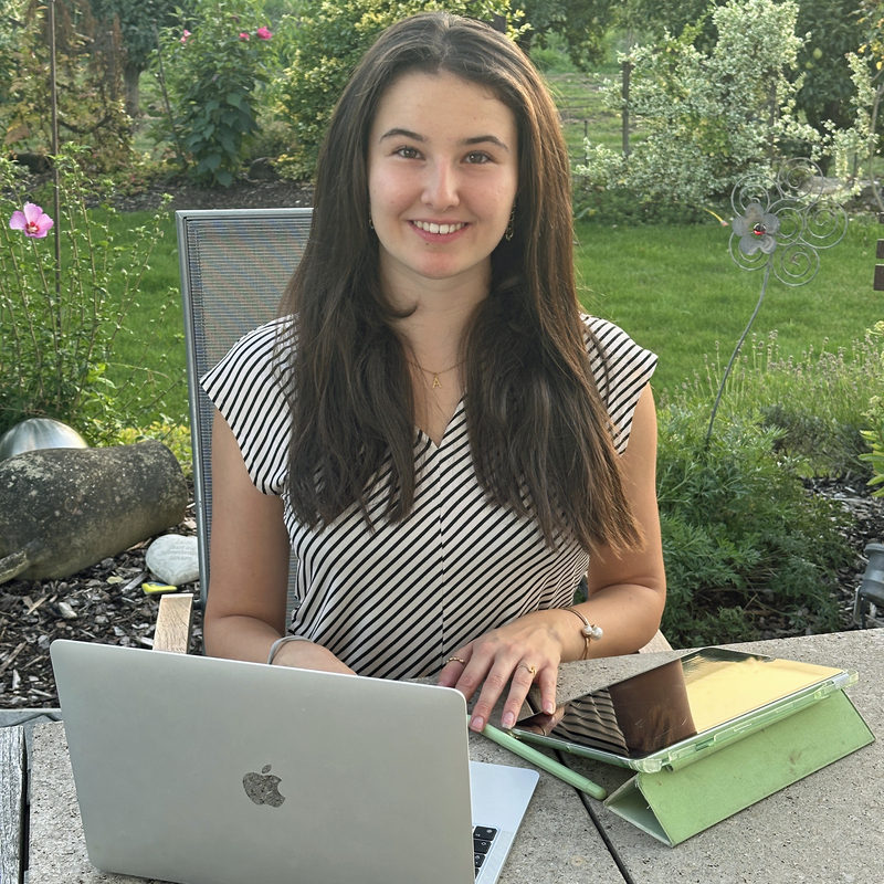 Eine junge Frau sitzt in einem Garten vor einem Laptop