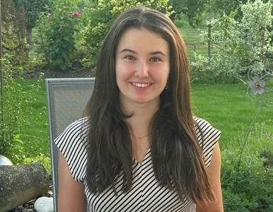 Eine junge Frau sitzt in einem Garten vor einem Laptop