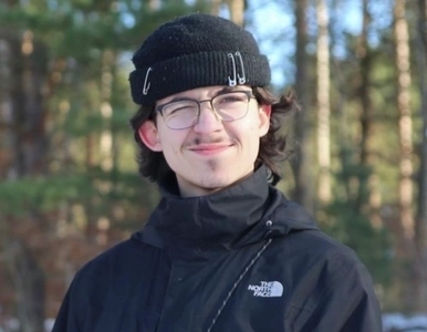 Porträt eines jungen Mannes in einer Schneelandschaft, der ein Auge zukneift