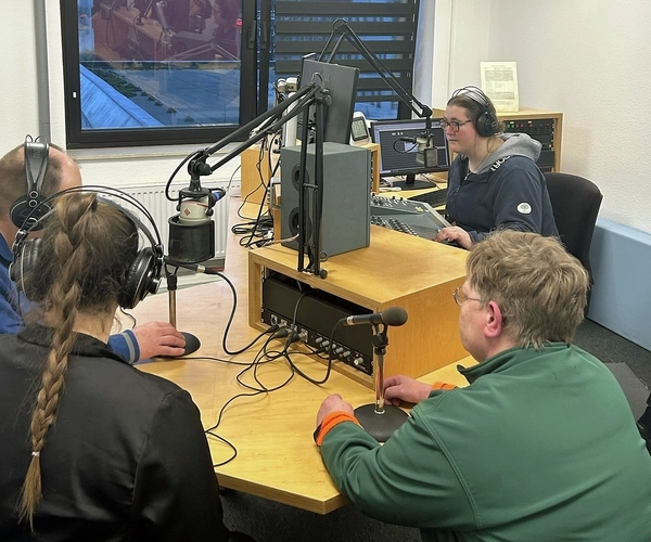 Vier Personen sitzen um einen Tisch und nehmen einen Podcast auf