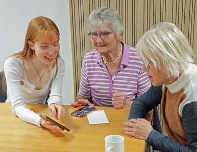 Eine junge Frau zeigt zwei Seniorinnen etwas auf dem Smartphone