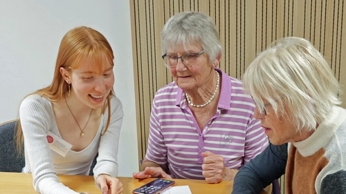Eine junge Frau zeigt zwei Seniorinnen etwas auf dem Smartphone