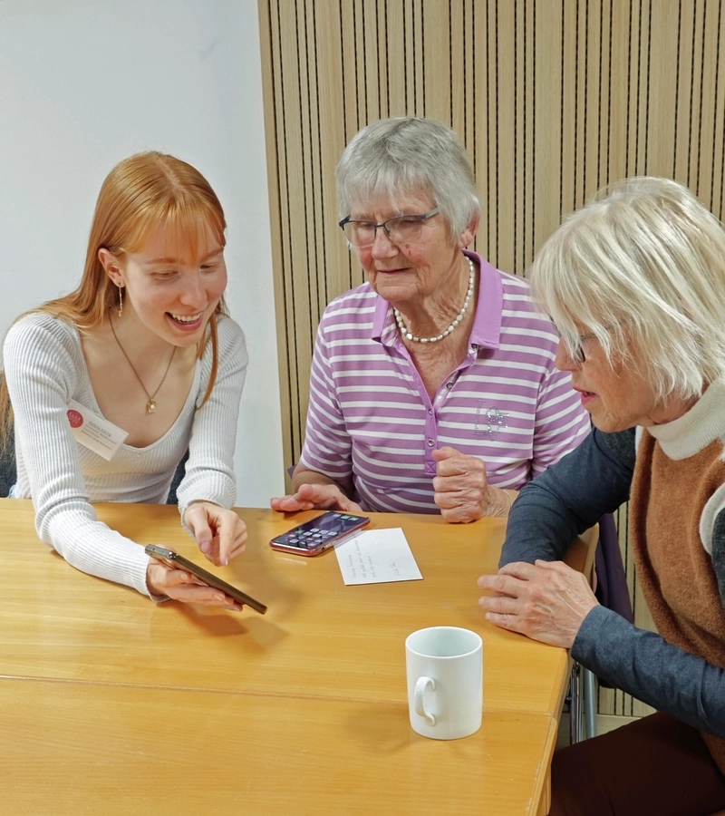 Eine junge Frau zeigt zwei Seniorinnen etwas auf dem Smartphone