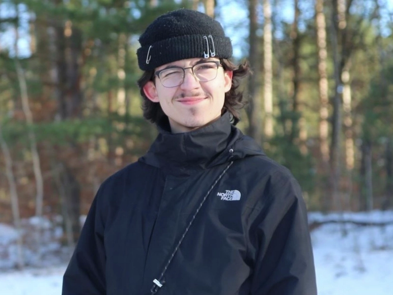 Porträt eines jungen Mannes in einer Schneelandschaft, der ein Auge zukneift