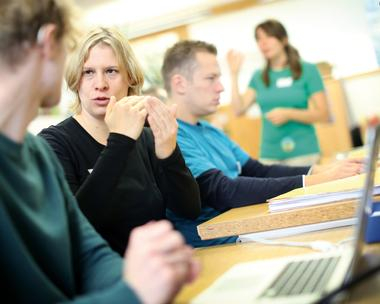 Eine Frau unterhält sich auf Gebärdensprache mit einem Mann, der neben ihr sitzt. 