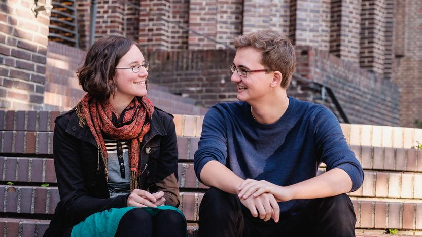 Carlotta und Jasper auf Steinstufen sitzend ins Gespräch vertieft.