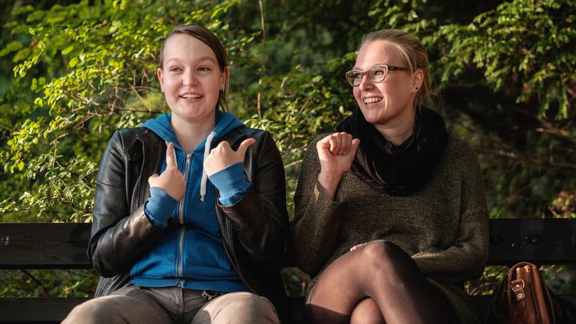 Ulrike und Frauke sitzen gemeinsam auf einer Bank im Park.