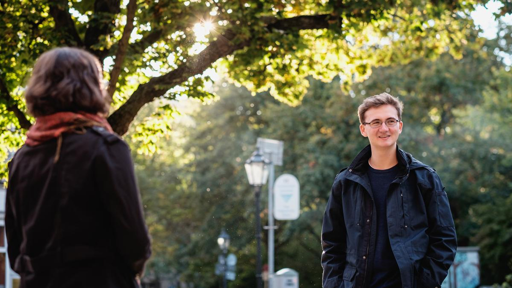 Carlotta und Jaspar stehen sich in einem Park gegenüber. Von Carlotta sieht man den Rücken, Jasper sieht man von vorne.