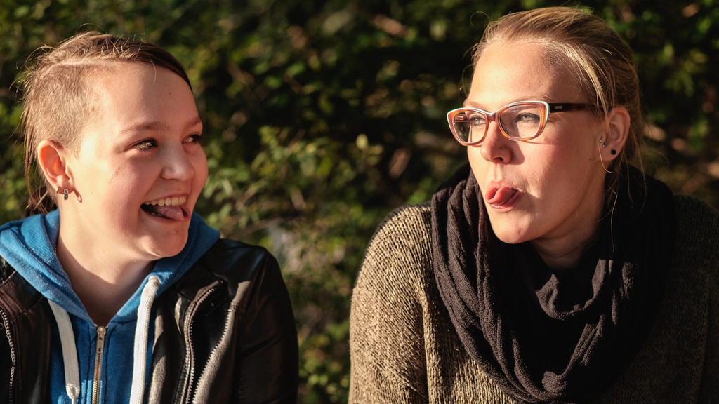 Frauke und Ulrike sitzen im Park nebeneinander und versuchen ihre Zungen zusammenzurollen.