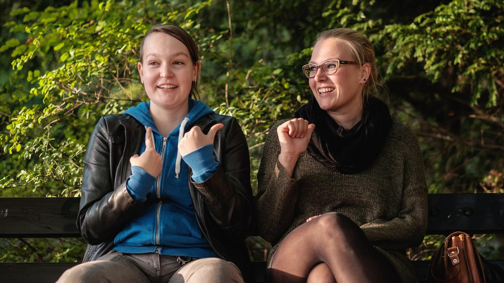 Ulrike und Frauke sitzen gemeinsam auf einer Bank im Park.