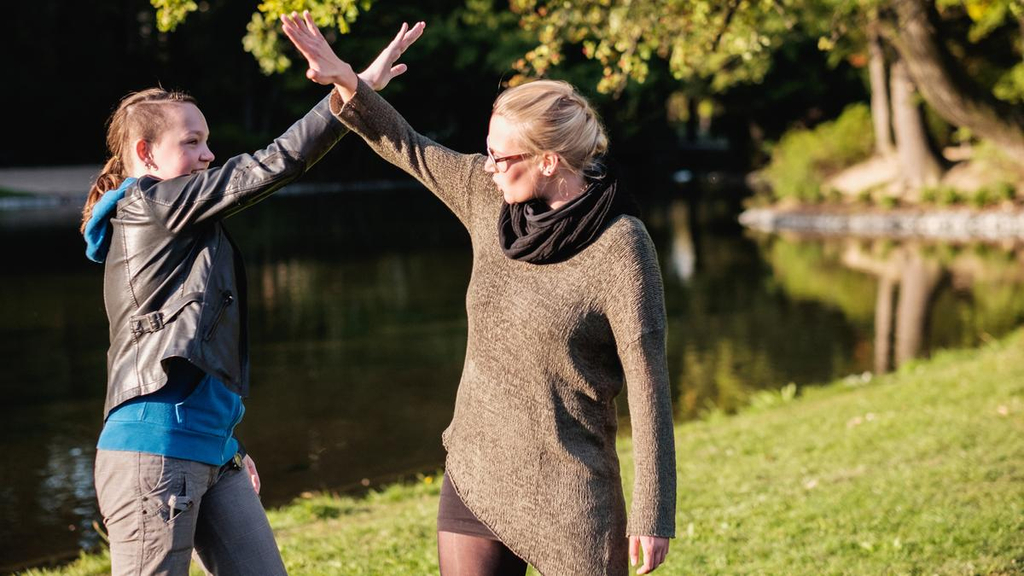 Frauke und Ulrike draußen im Grünen, ihre nach oben gestreckten Arme überkreuzen sich.