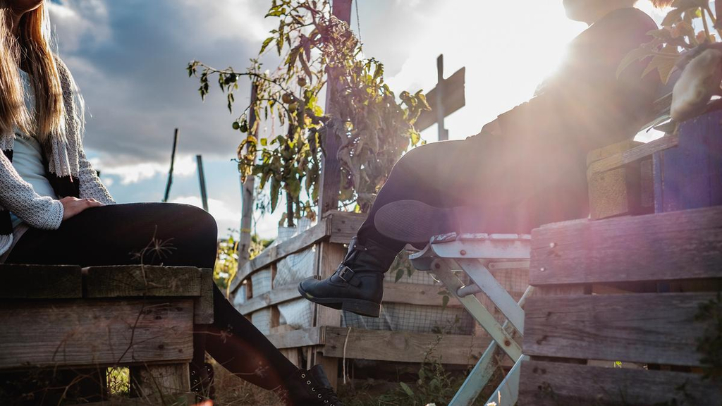 Jacqueline und Nicole sitzen auf Holzkisten und machen Pause, man sieht nur die Körper und baumelnden Beine, nicht die Gesichter.