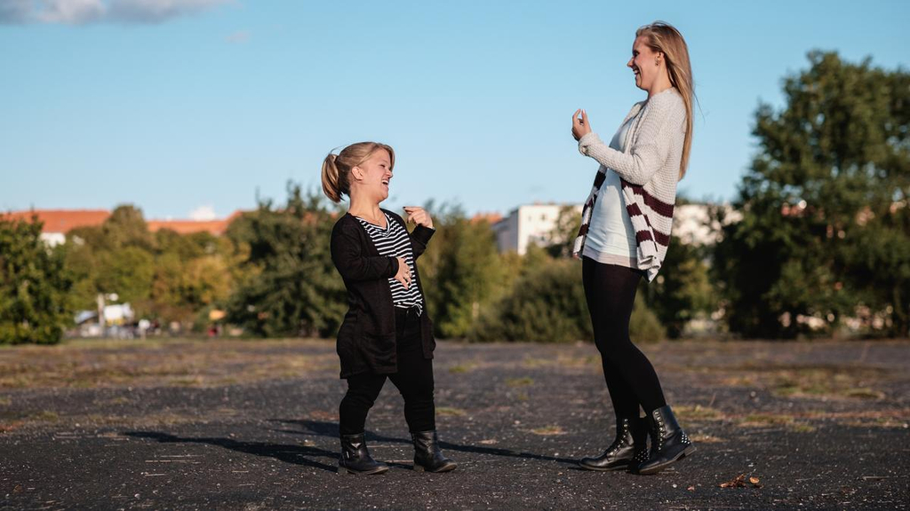 Jacqueline und Nicole stehen sich auf einer Straßen gegenüber und lachen sich herzlich an.