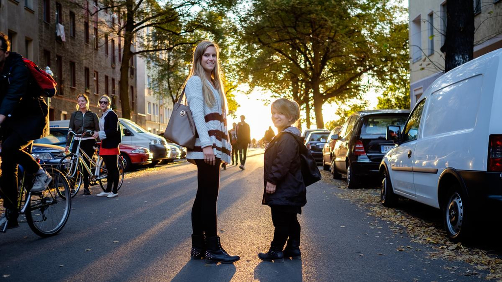 Nicole und Jacqueline stehen sich auf einer Straße gegenüber und lächeln in die Kamera. Im Hintergrund sieht man die untergehende Sonne.