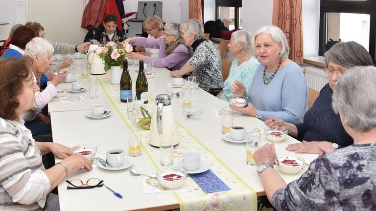 Eine Gruppe von älteren Menschen sitzen an einem Tisch und essen gemeinsam.