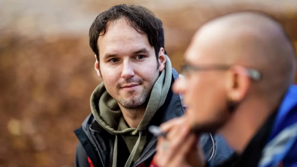 Zwei Männer sitzen im Gespräch nebeneinander, der Mann im Vordergrund ist unscharf fotografiert.