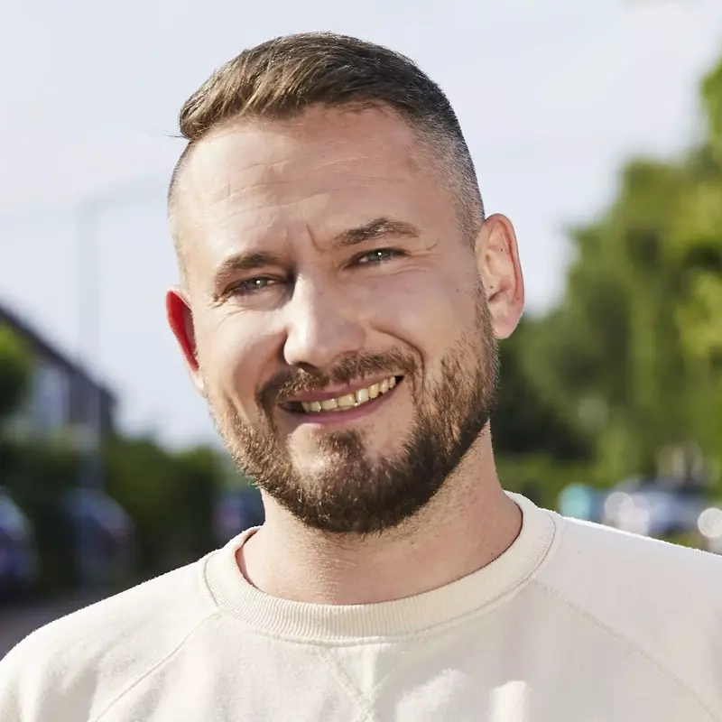 Ein Mann mittleren Alters mit blondem kurzem Haar und Vollbart. Er lächelt in die Kamera.