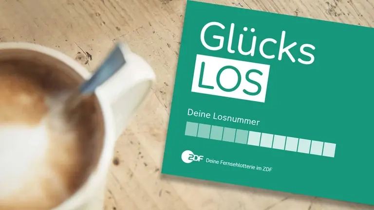 Ein Glücks-Los liegt auf einem Tisch. Daneben steht eine Tasse Kaffee.