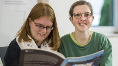 Cathrin Öhler liest mit einer anderen Frau in einem Buch.