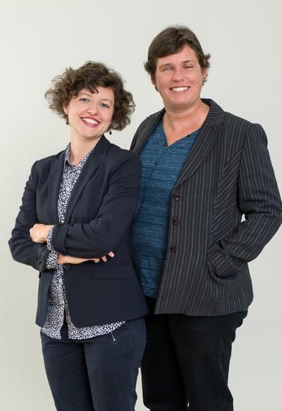 Zwei Frauen stehen lächelnd nebeneinander, eine ist blind. 