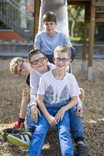 Vier Jungs sitzen hintereinander auf einer Rutsche und lachen in die Kamera