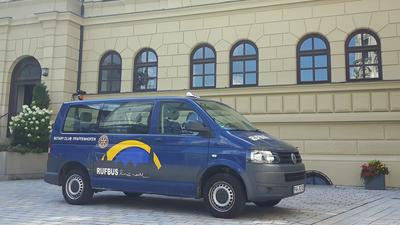 Ein blauer Kleinbus mit der Aufschrift Rufbus steht vor einem großen Gebäude