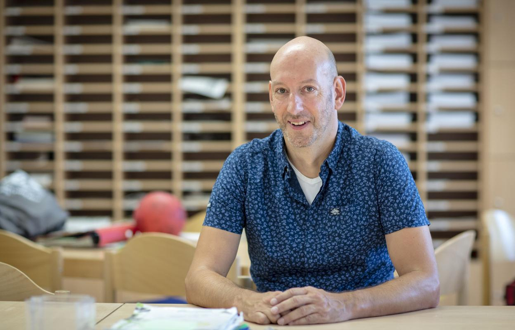 Stefan Richter sitzt im Lehrerzimmer und lächelt in die Kamera. Im Hintergrund sieht man viele Postfächer.