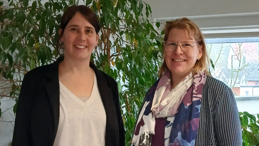 Lena Haas-Möldner und Manuela Bittner stehen in einem Büro, lächeln, hinter ihnen steht eine große Zimmerpflanze