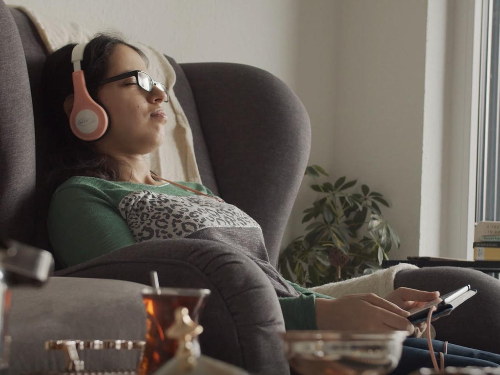 Eine junge Frau sitzt mit geschlossenen Augen und Kopfhörern in einem Sessel