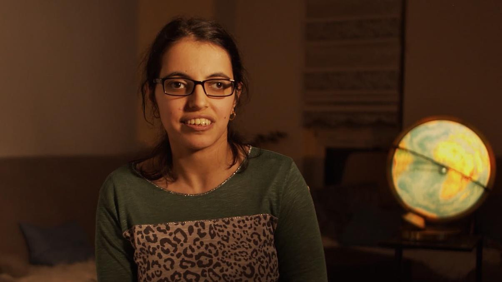 Eine junge Frau sitzt in einem abgedunkelten Zimmer, im Hintergrund leuchtet ein Globus