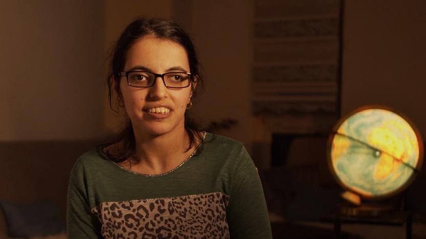 Eine junge Frau sitzt in einem abgedunkelten Zimmer, im Hintergrund leuchtet ein Globus