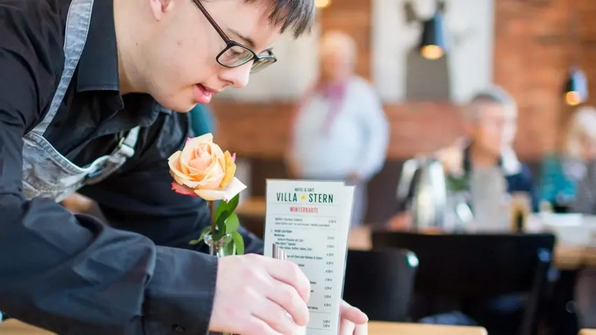 Ein Mann mit Behinderung richtet die Tischdeko in einem Restaurant.