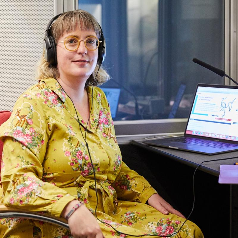 Eine Frau mit Kopfhörern sitzt vor einem Mikrofon am Laptop.