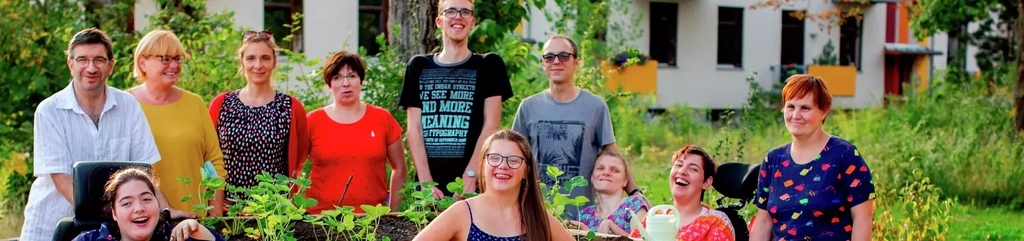 Eine Gruppe von Menschen mit und ohne Behinderung steht um ein Hochbeet, das sie gerade bepflanzt haben. Alle lächeln.