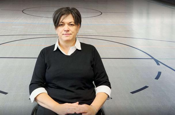 Katja Lüke, eine Frau mit dunklen, kurzen Haaren, sitzt in ihrem Rollstuhl in einer Sporthalle.