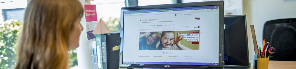 Eine Frau sitzt vor dem Computer. Auf dem Bildschirm ist die Starteseite des Aktion Mensch-Familienratgebers zu sehen.