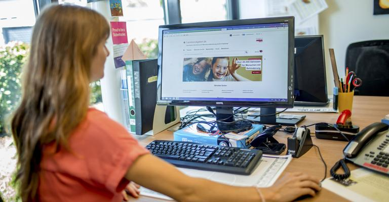 Eine Frau sitzt vor dem Computer. Auf dem Bildschirm ist die Starteseite des Aktion Mensch-Familienratgebers zu sehen.