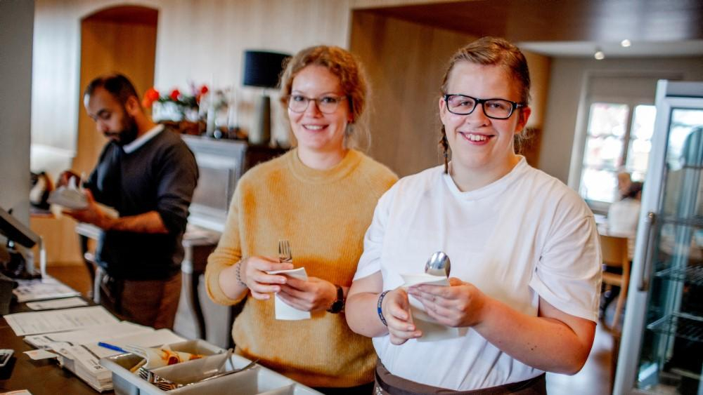 Zwei Frauen in einem Gastrobetrieb wickeln Besteck in Servietten