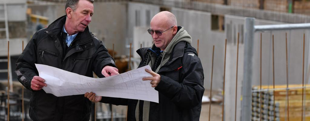 Zwei Männer stehen auf einer Baustelle und schauen sich gemeinsam einen Plan an.