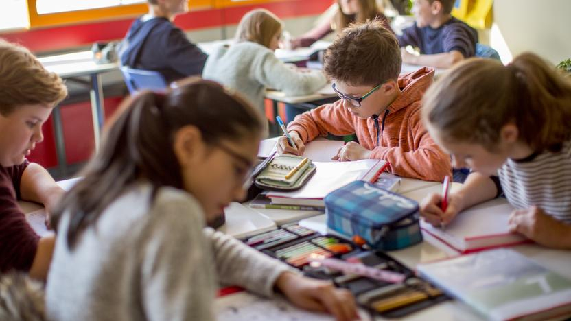 Mehrere Kinder sitzen in der Klasse der Albert-Einstein-Schule in Bad Schwalbach um einen Tisch herum und schreiben etwas in ihre Hefte. 