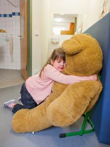 Mädchen schmust in Klassenraum mit riesigem Stoff-Bär.