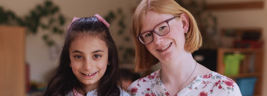 Eine junge Frau mit Downsyndrom und ein Mädchen im Kindergartenalter stehen lächelnd nebeneinander