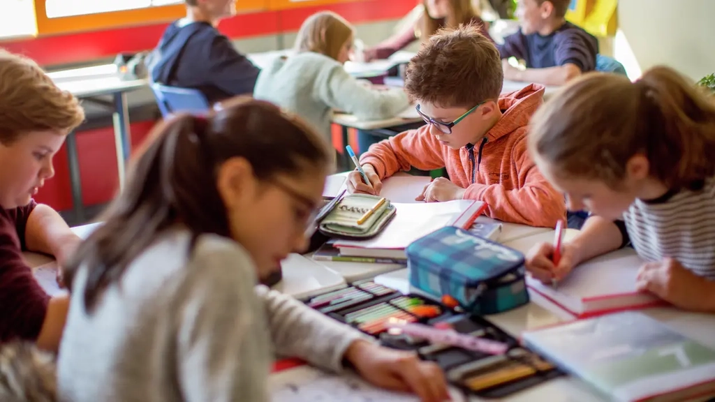 Mehrere Kinder sitzen in der Klasse der Albert-Einstein-Schule in Bad Schwalbach um einen Tisch herum und schreiben etwas in ihre Hefte.