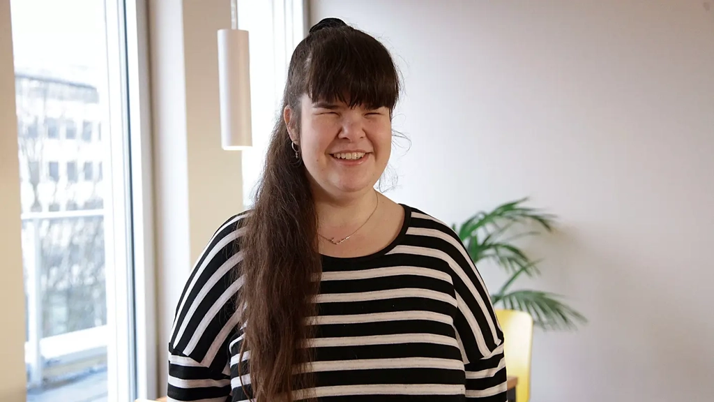 Eine junge Frau mit langem dunklem Pferdeschwanz und Ringelshirt lächelt in die Kamera.