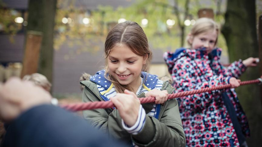 Zwei Mädchen balancieren und halten sich an einem dicken Seil fest. 