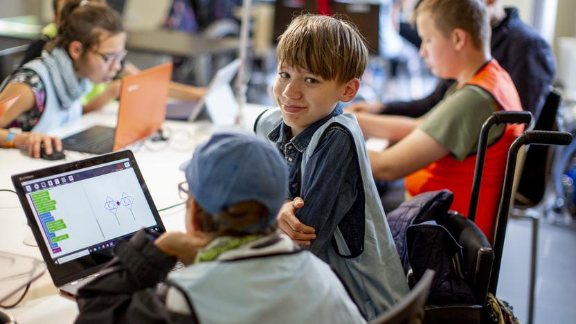 Zwei Jungen sitzen in einem Klassenzimmer gemeinsam vor einem Laptop. Einer der Jungen sitzt im Rollstuhl.