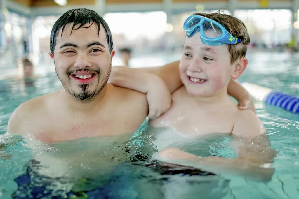 Zwei Jugendliche sind zusammen in einem Schwimmbecken. Einer der beiden Jungen hat eine Behinderung, der andere nicht. Er trägt eine Schwimmbrille auf dem Kopf.