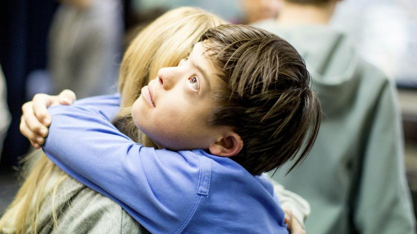Ein Junge mit Behinderung umarmt eine Frau auf der Bühne.