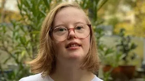 Porträt einer jungen Frau mit Down-Syndrom. Sie trägt ein T-Shirt mit der Aufschrift: #Inkluencerin