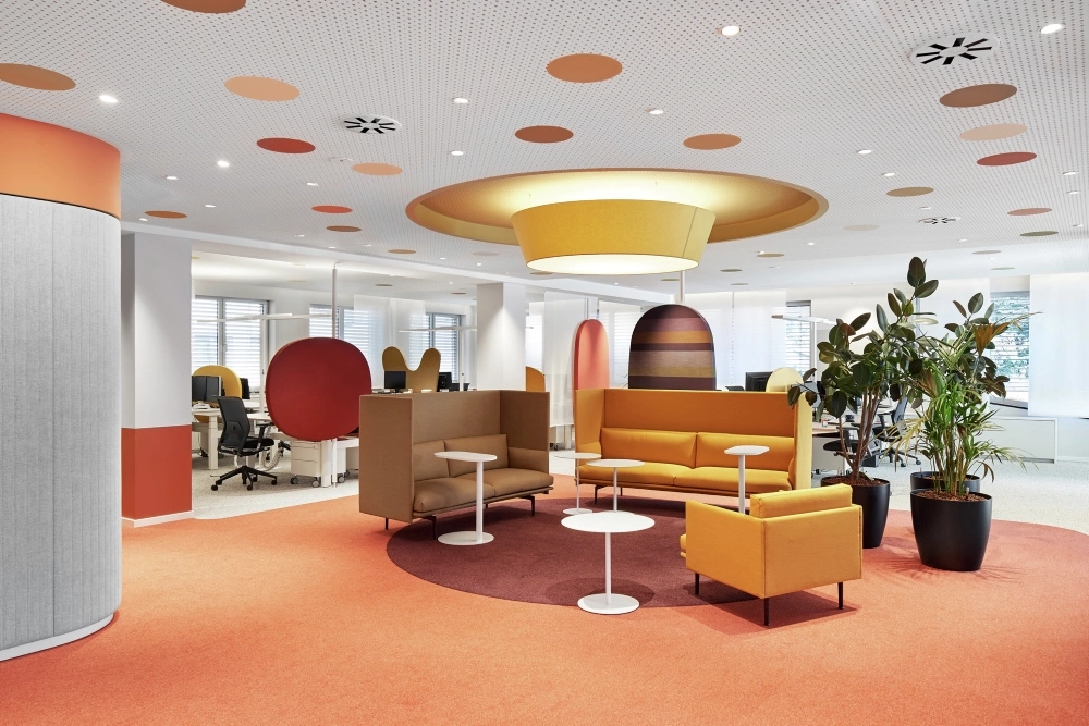 Ein Bild der Büroräume der Aktion Mensch mit orangenem Teppichboden und gelben Möbeln in einer Sitzgruppe.